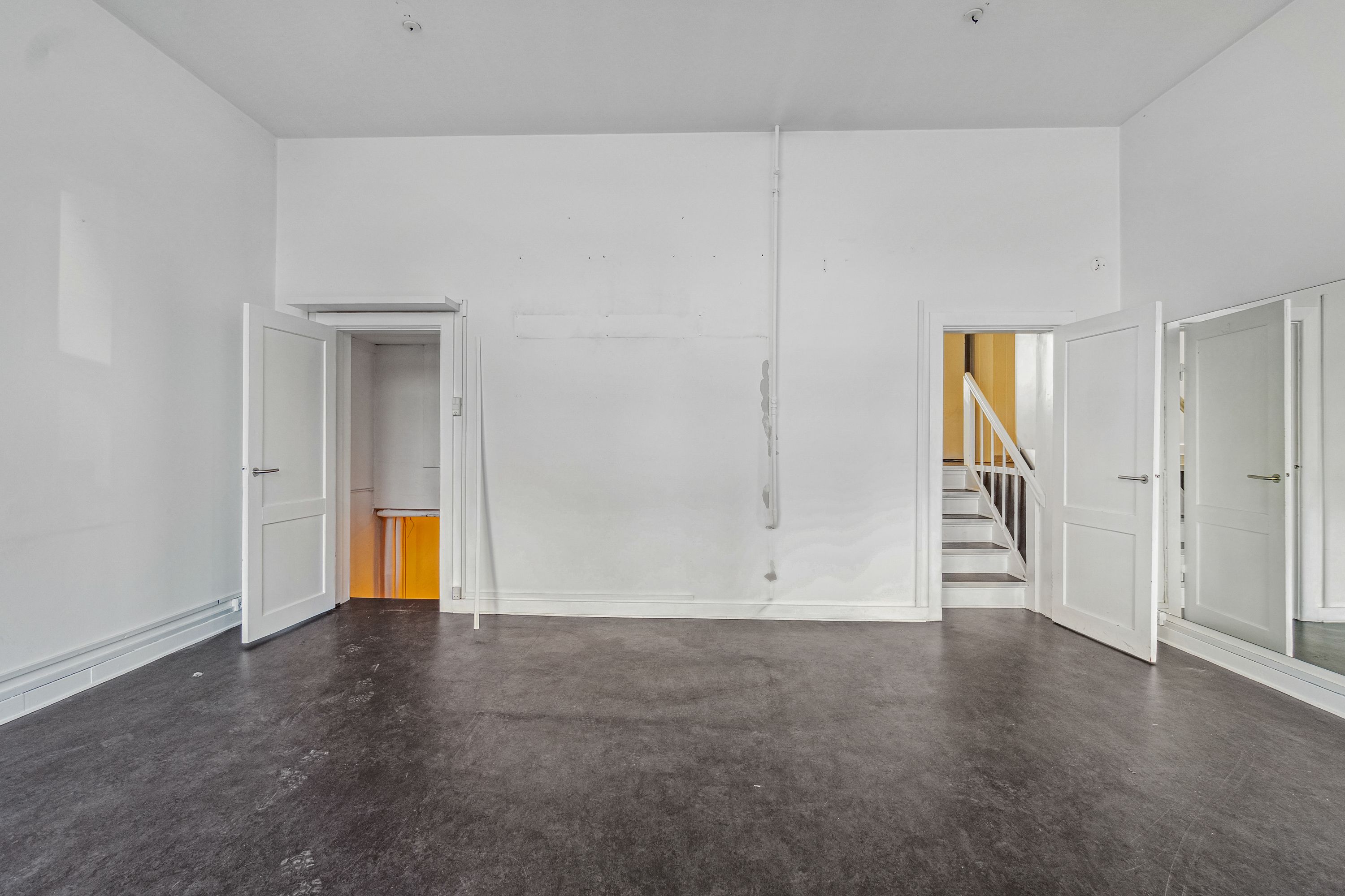 Udlejningslejlighed i Frederiksberg med fire åbne døre og to stige i baggrunden, gulvet er mørkegråt og væggene er hvide