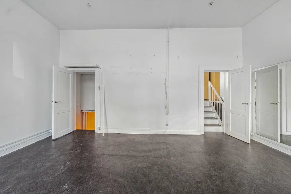 Udlejningslejlighed i Frederiksberg med fire åbne døre og to stige i baggrunden, gulvet er mørkegråt og væggene er hvide
