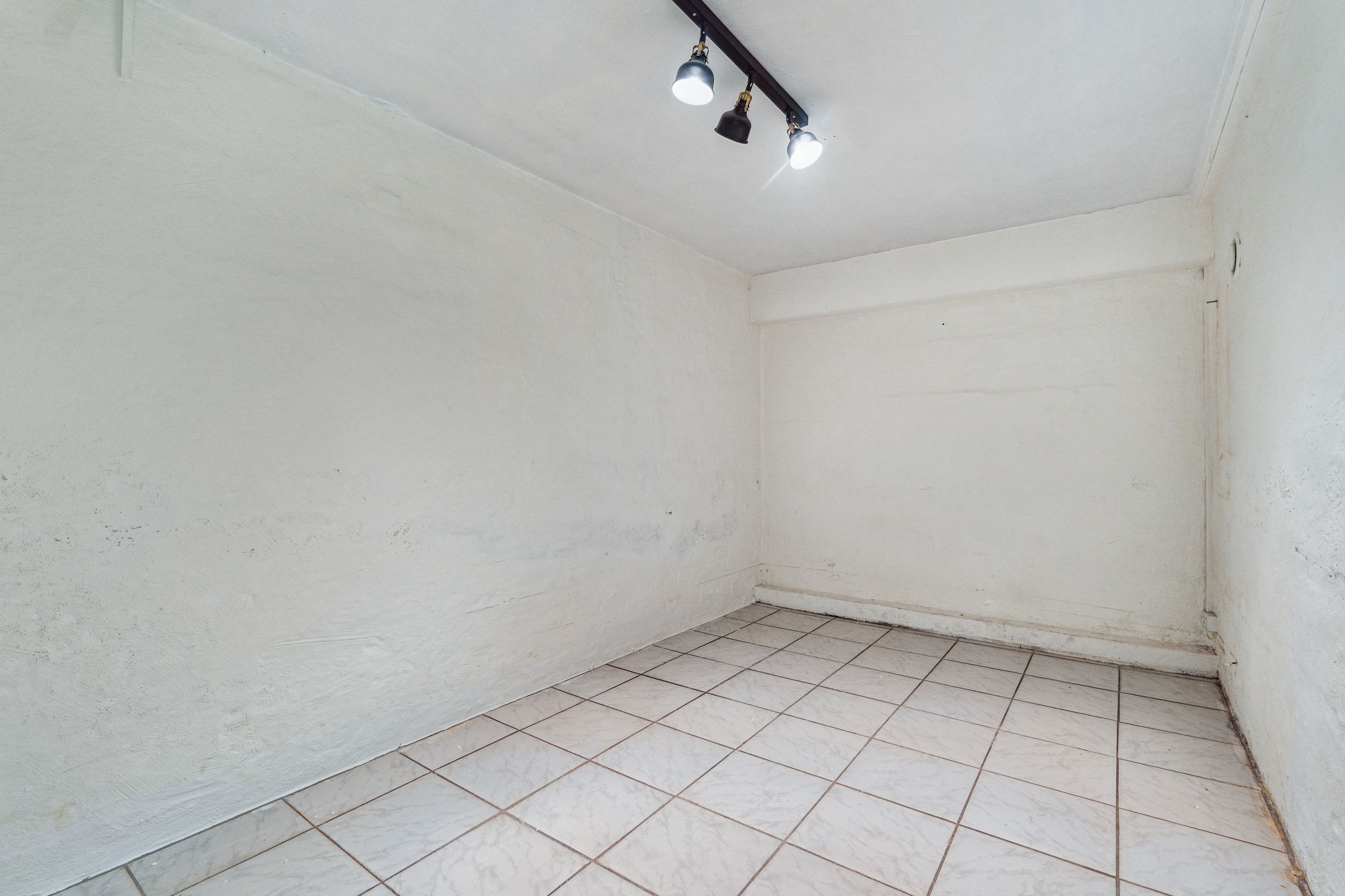 En stor, lysegrå, ubenyttet butikslokale med smukke gulvfliser og tre hængelys på loftet. Lokalet ligger på Søndre Fasanvej 45, st. 2, Frederiksberg.