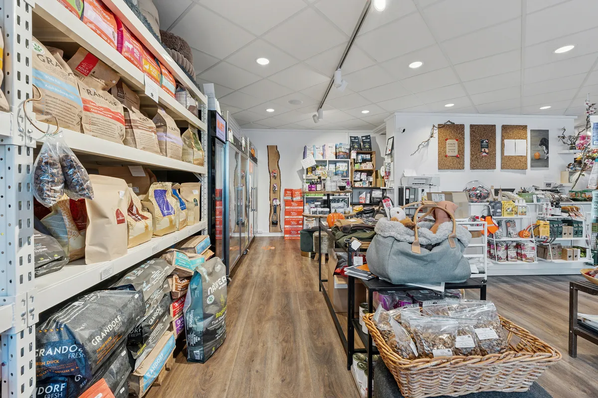 Alt-tekst: Lys butik med trægulv og høje hylder med Grandorfe-foder og snacks til kæledyr, en gryde med snacks og en pude på bordet