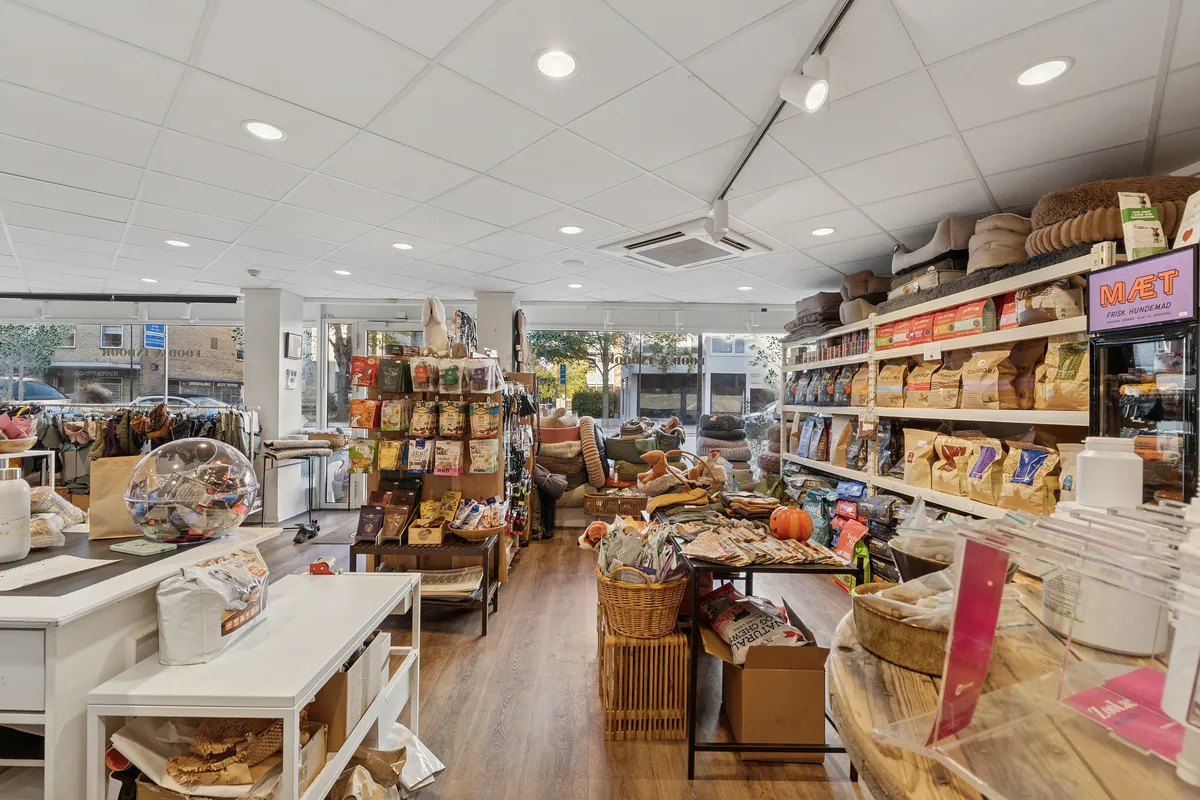 En moderne butik med en bred facade og to store vinduer, indrettet med hylder, kurve og trægulv, og udstyret med kvalitetsprodukter og udstyr