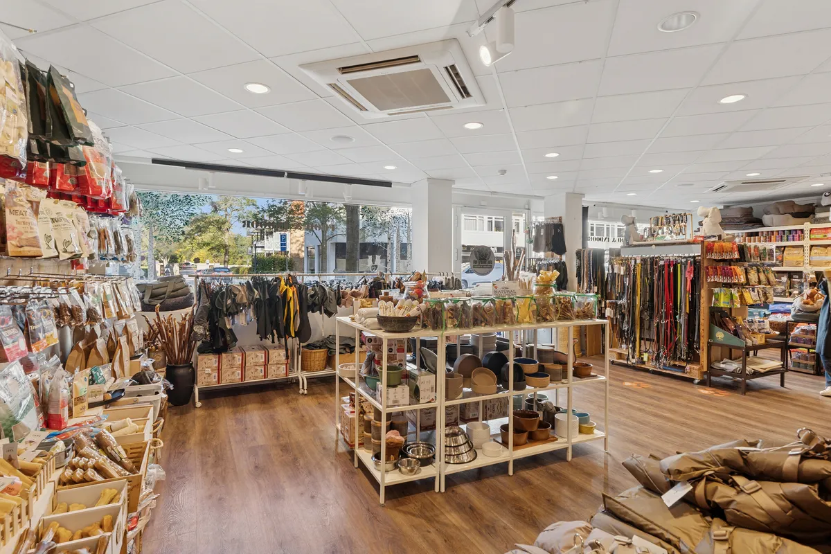 En køkkenudstyrsbutik med trægulv og hvide hylder, flere varer og produkter i udsalg, en person står ved en købmandsvogn, og der er flere varer på gulvet