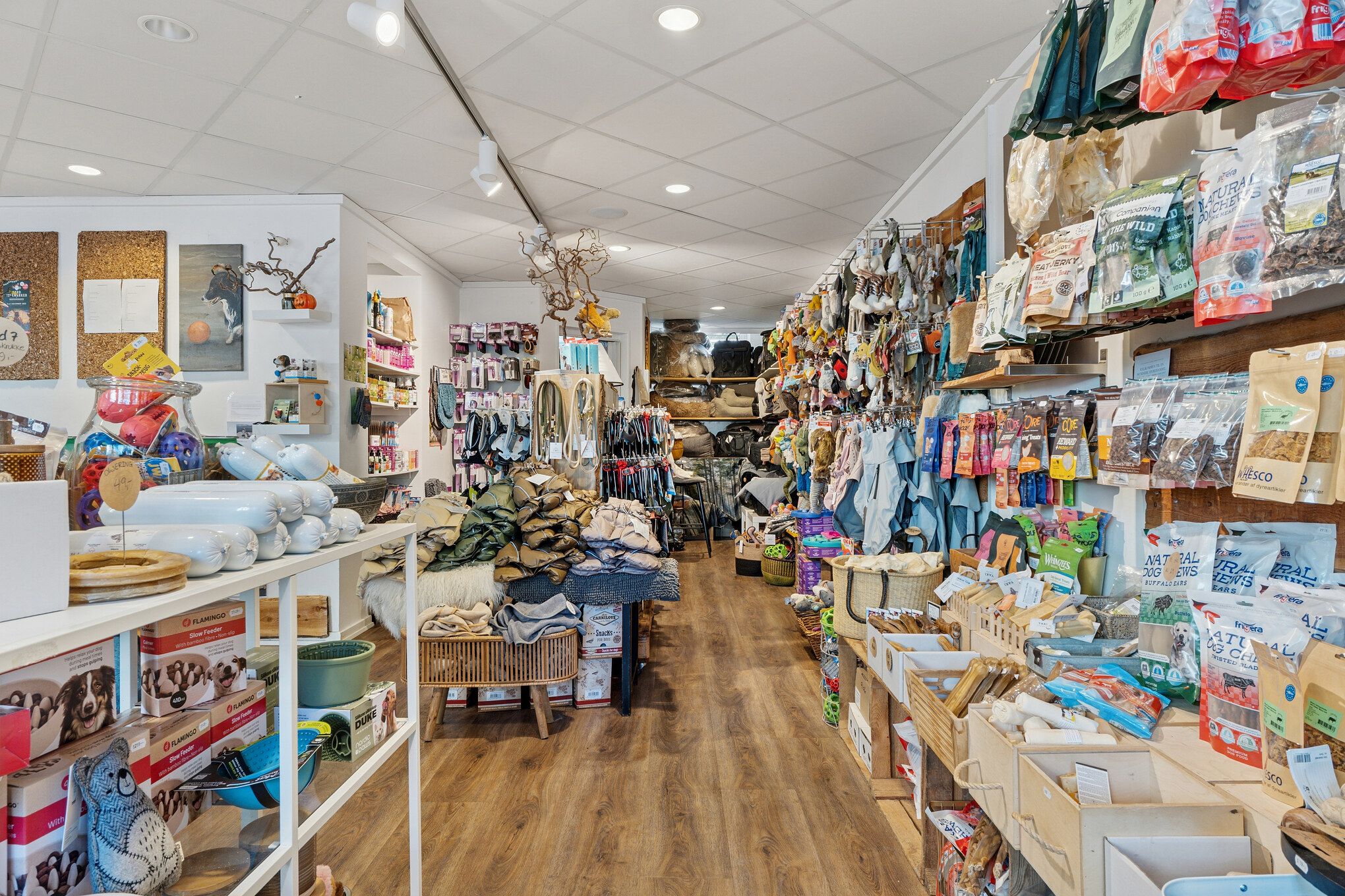 Lyst og indbydende butikslejemål med god eksponering og fleksibel indretning, inkluderende trægulve, hængende produkter, og forskellige kategorier af varer