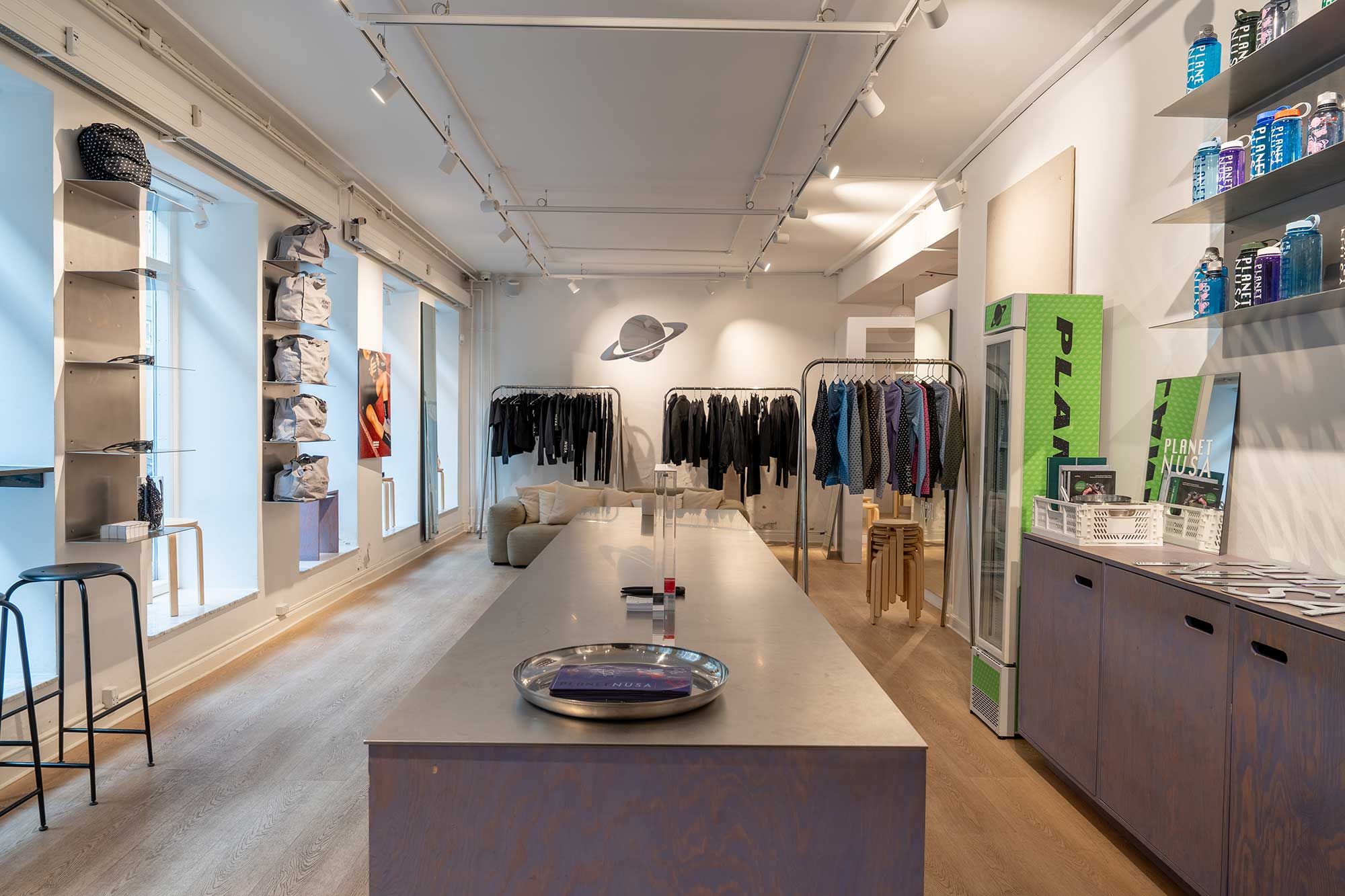 Lys og rummelig butik med salgspuljer og sofaer i Latinerkvarteret. Flad loft og gulv med lysepunkter og produkter på hylder.