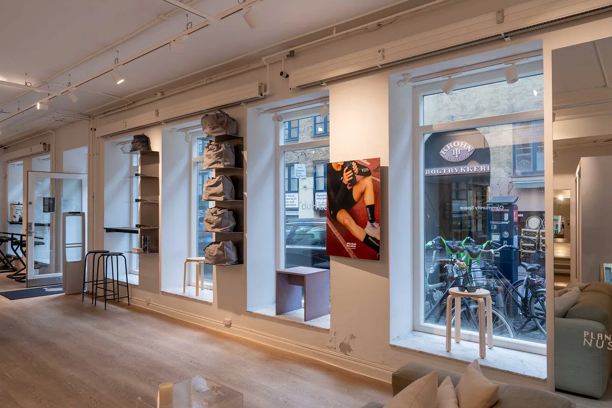 Markant butikslejemål med stort vindue og møbler i Latinerkvarteret, køkken og loftsrum til leje, hyggeligt møbleret interiør med lyse farver og moderne design.