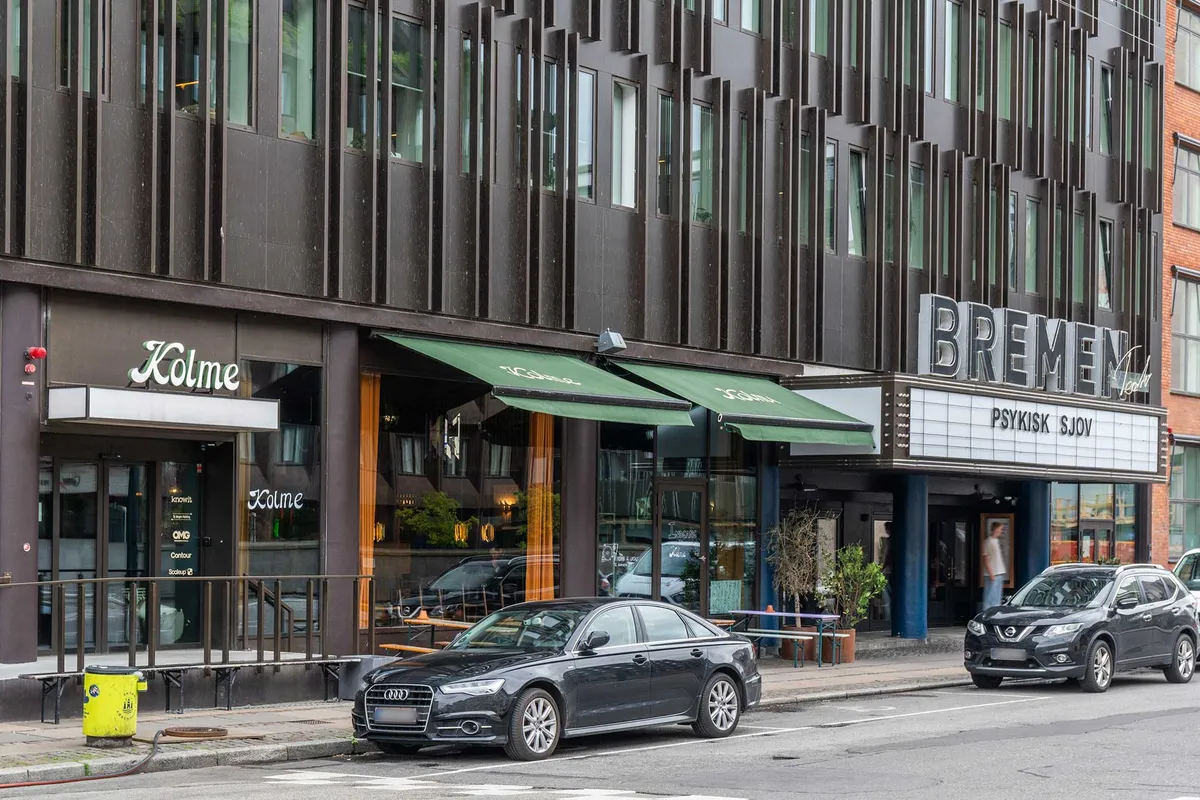 To sorte biler er parkeret udenfor et bygningskompleks med et kinesisk navn og en cafe med grønne kulisserne