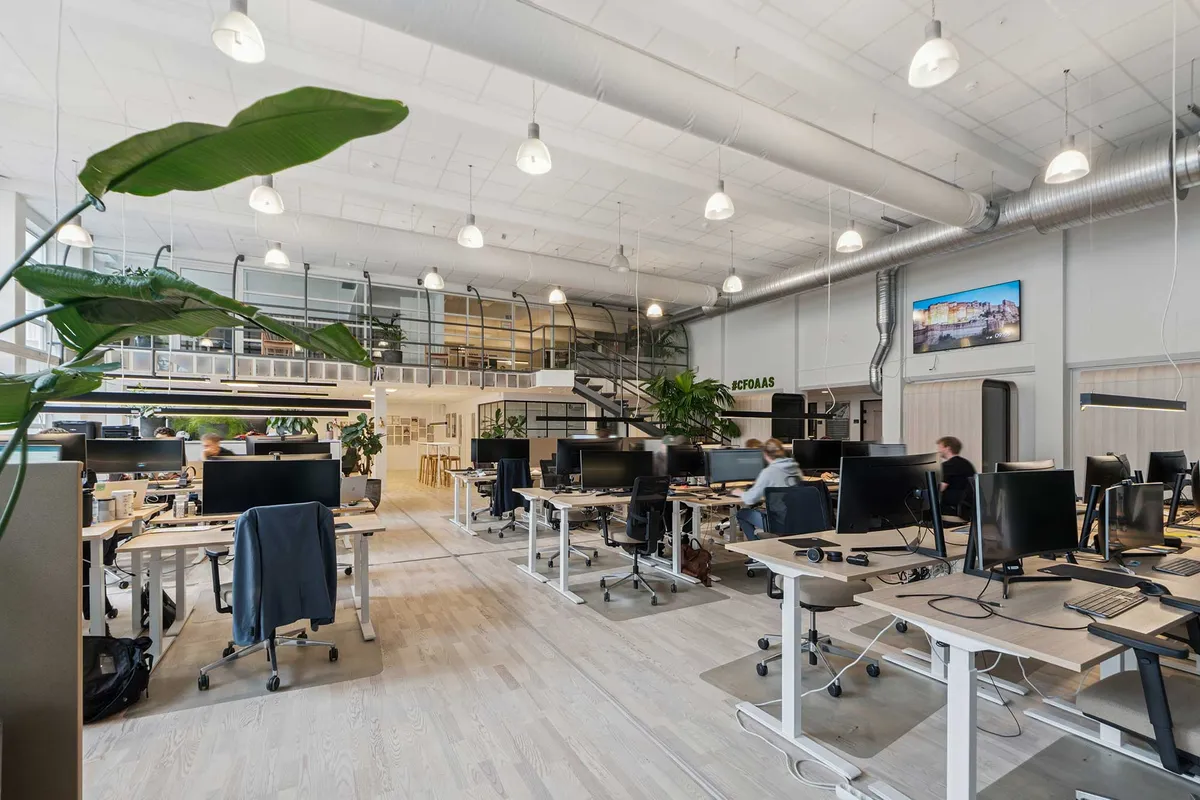 Kontor med højt til loftet, lyse loftslampe, store vinduer og en åben værkstedstil. Der er fællesområder og en restaurant.