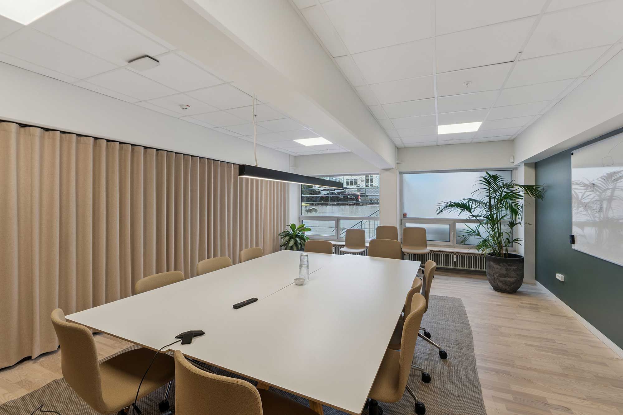 Kontorrum med højt til loftet og adgang til personalerestaurant og café. Mødelokale med hvide borde og stole samt smukke plante og whiteboard.