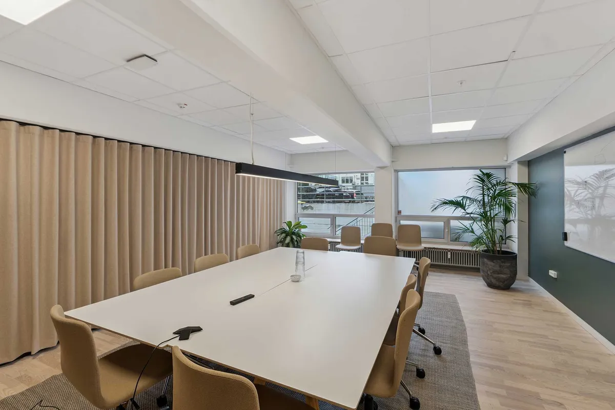 Kontorrum med højt til loftet og adgang til personalerestaurant og café. Mødelokale med hvide borde og stole samt smukke plante og whiteboard.