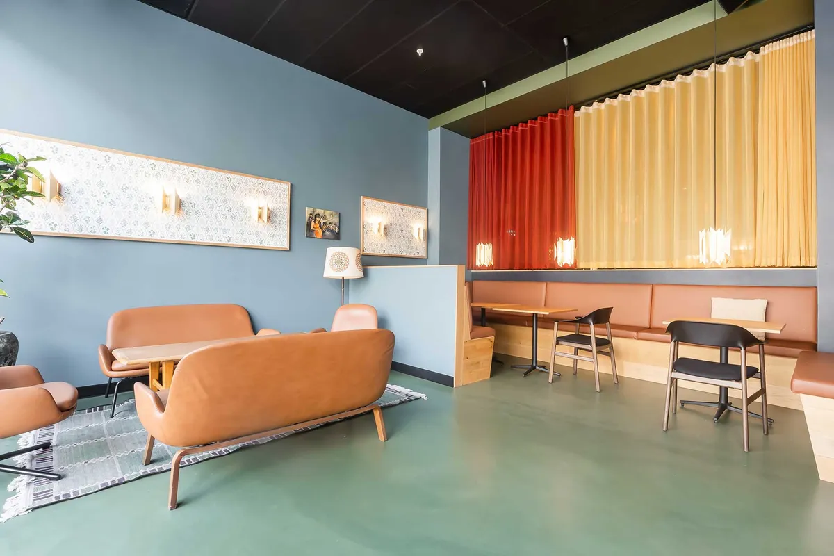 Kontorområde med lyse vægge, røde og gule gardiner, to lange sofaer, flere stole og to mindre borde, møbler med moderne design og en stor plante i lysegrå farve