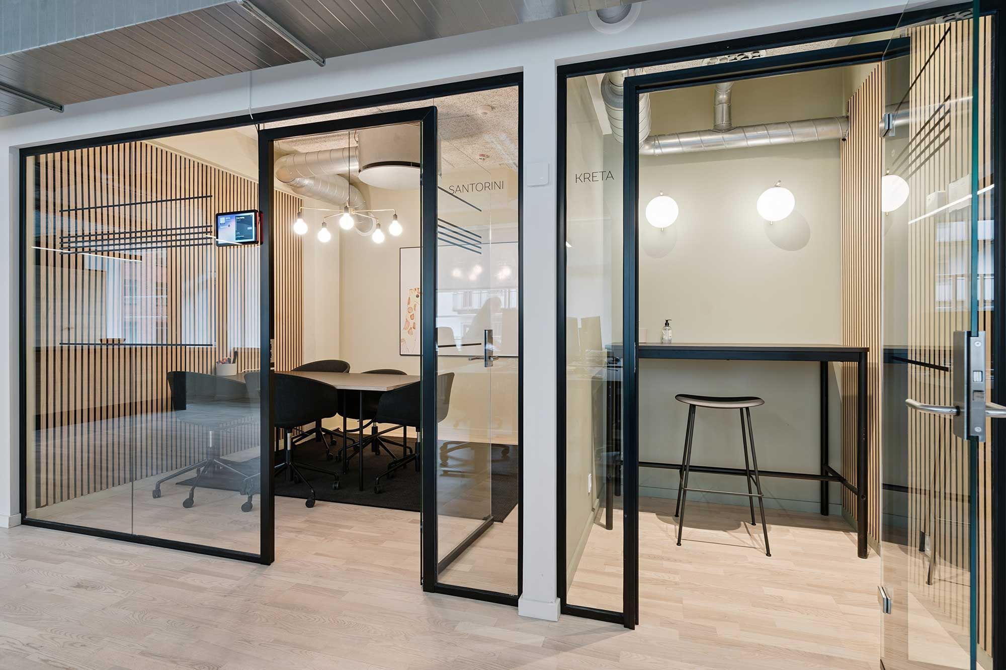 Et moderne kontorlokal med glasvægge og møbler i sort og brun, oplyst af lyse loftslamper og gulvbelægning