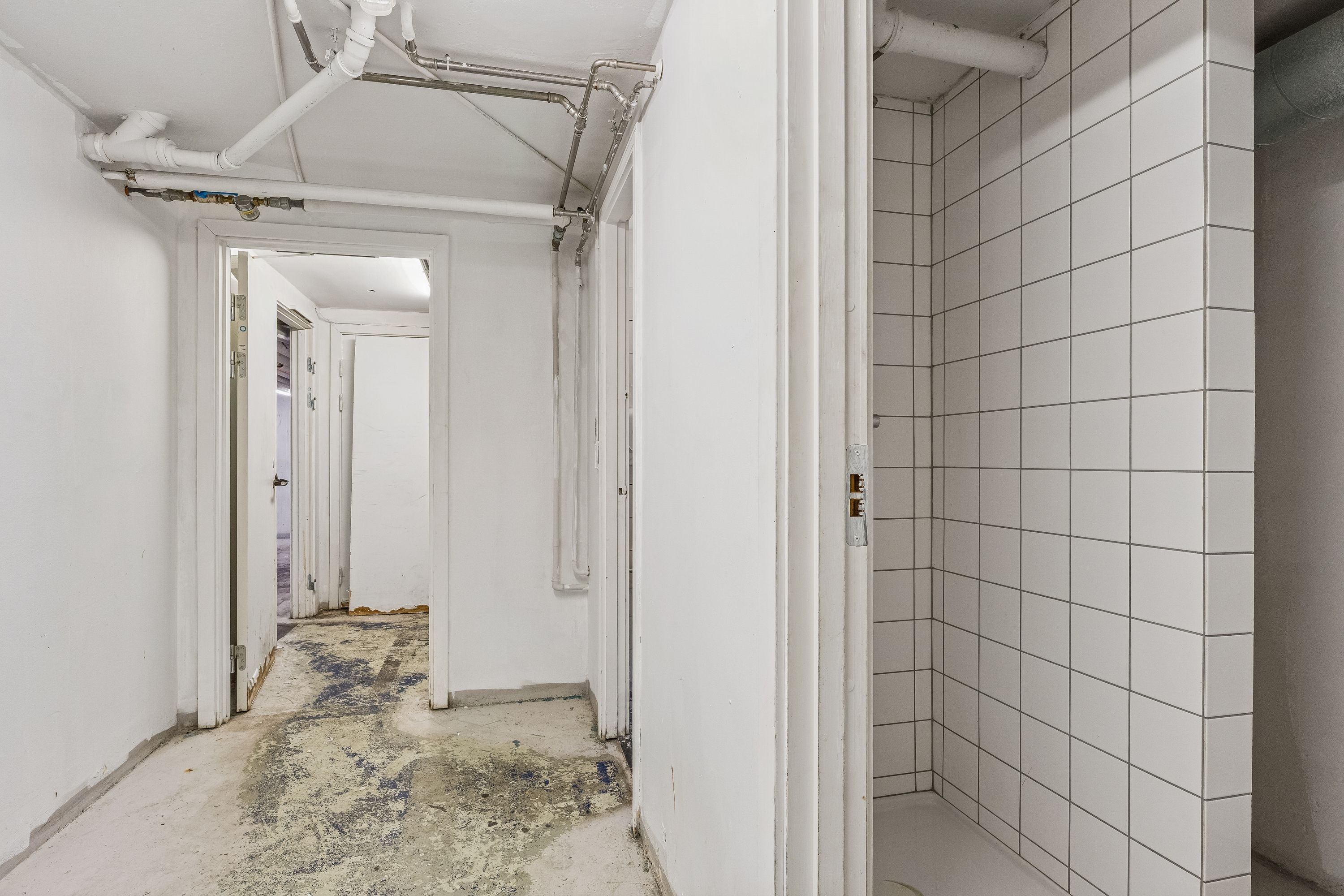 Lang række af hvide vægge og gulve i en lejlighedsgang, hvor der er tilsluttede rør og ventiler i loftet