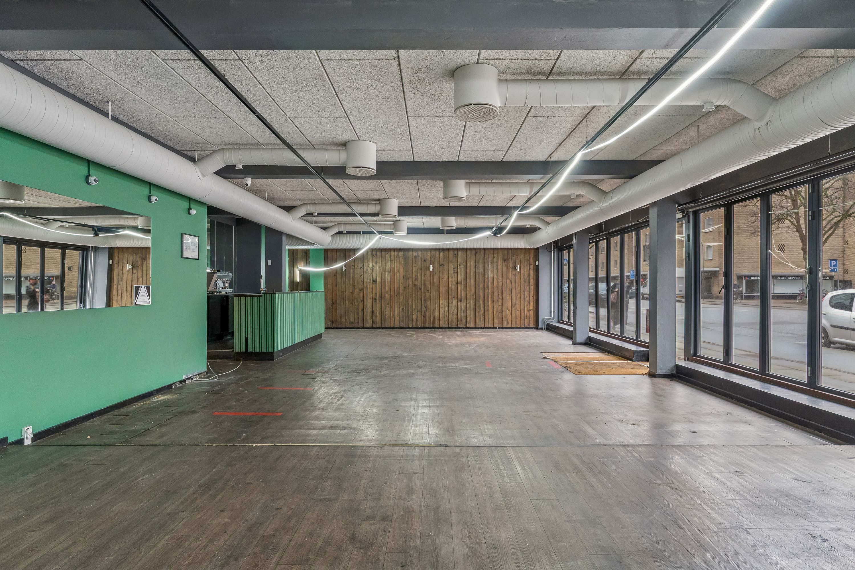 Store tomt med åbent gulv og store ruder samt rør i loftet og en grøn væg med en spejl og kameraer