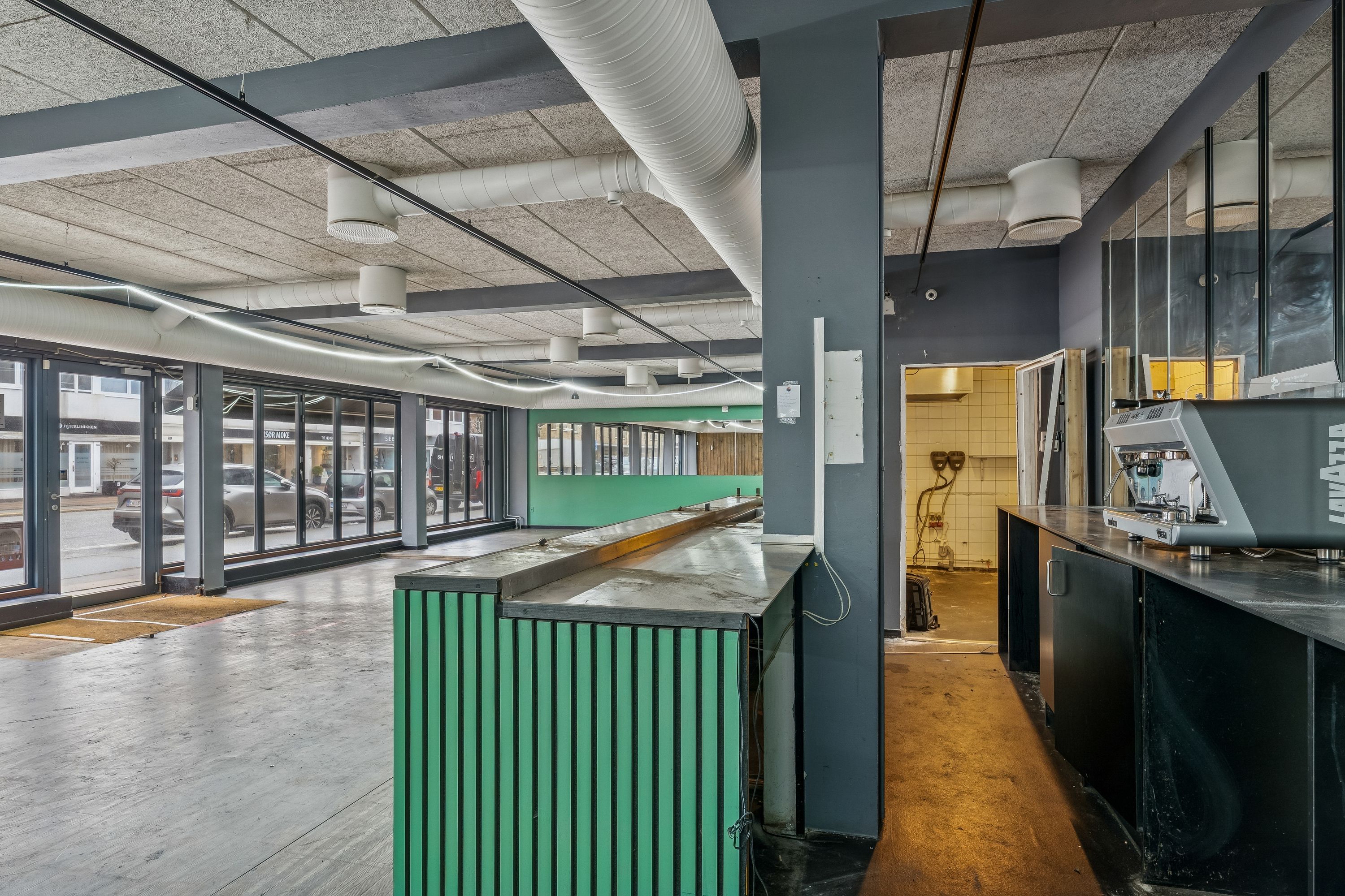 En lukket restaurant med en grøn søjle og en kaffemaskine samt et glasvindu med udsigt til en parkeringsplads med biler