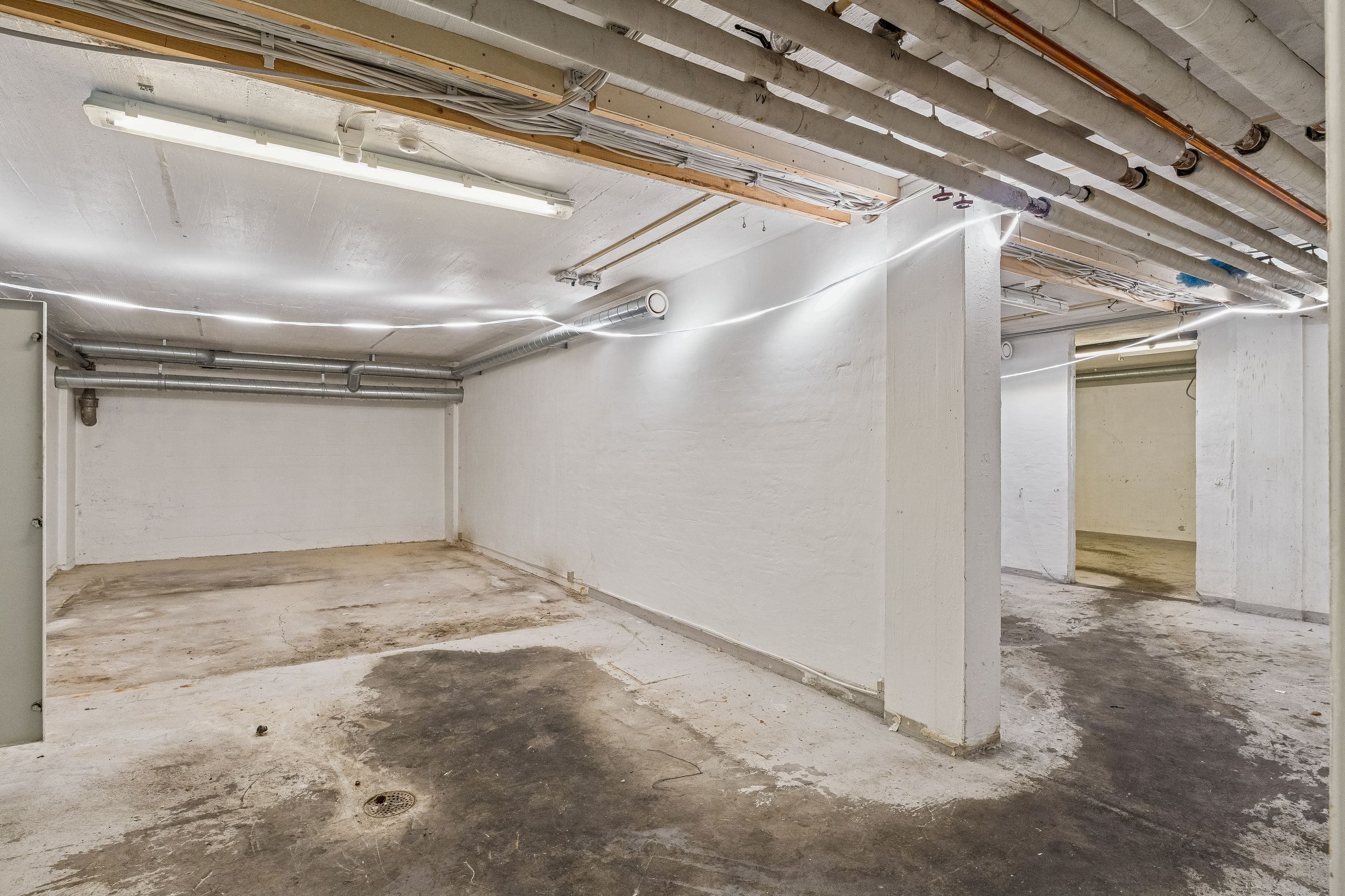 En tom underjordisk parkeringskælder med hvide vægge, lyse og røre. Der er to store højdekolonner og røre på gulvet.