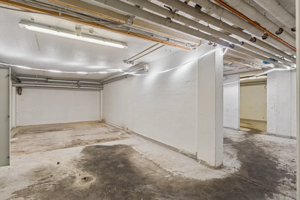 En tom underjordisk parkeringskælder med hvide vægge, lyse og røre. Der er to store højdekolonner og røre på gulvet.