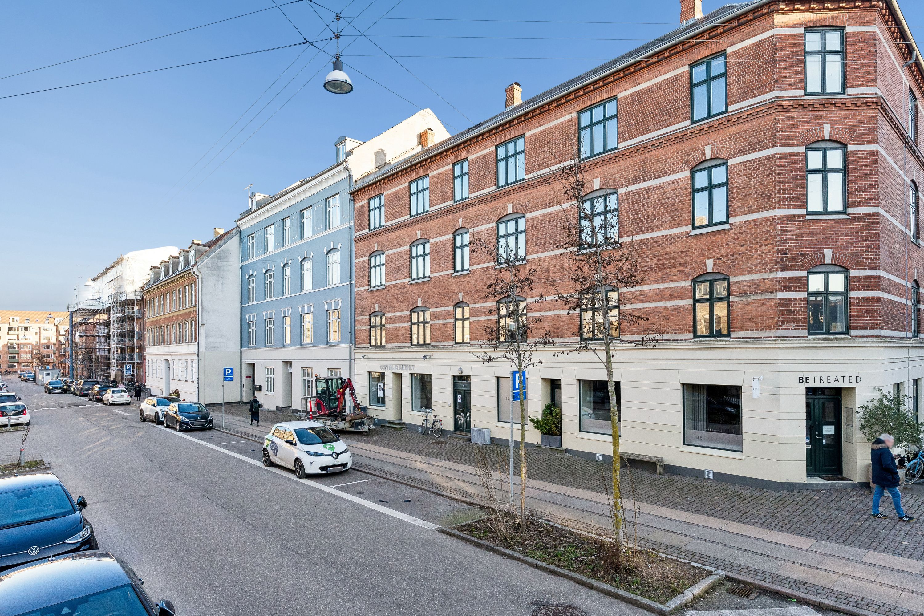 Menighedsgården med røde mursten og hvide striber ligger på Landskronagade 13, og øverste etage er til leje. Der er skrift med Be Treated og søjler med lysekroner og planter udenfor.