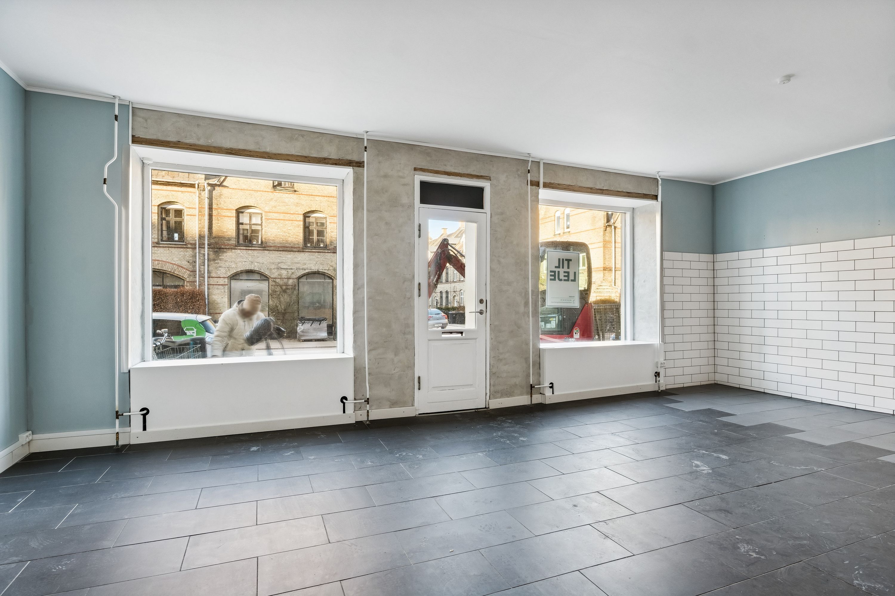 En nyrenoveret lejlighed med to store vinduer og hvide kakeløg mod væggen. To store vinduesrammer og en hvid dør er på plads. Der er lige blevet lægget gulv.