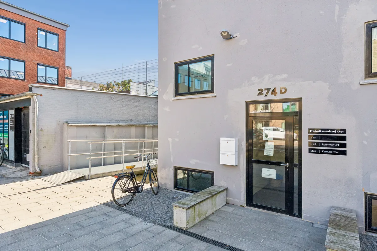 Kontoret på Frederikssundsvej 274D har en glasdør og et skriftstykke med navnene Sal og Reformer CPH. En cykel står foran døren, og der er en skrånende gang i forgrunden.