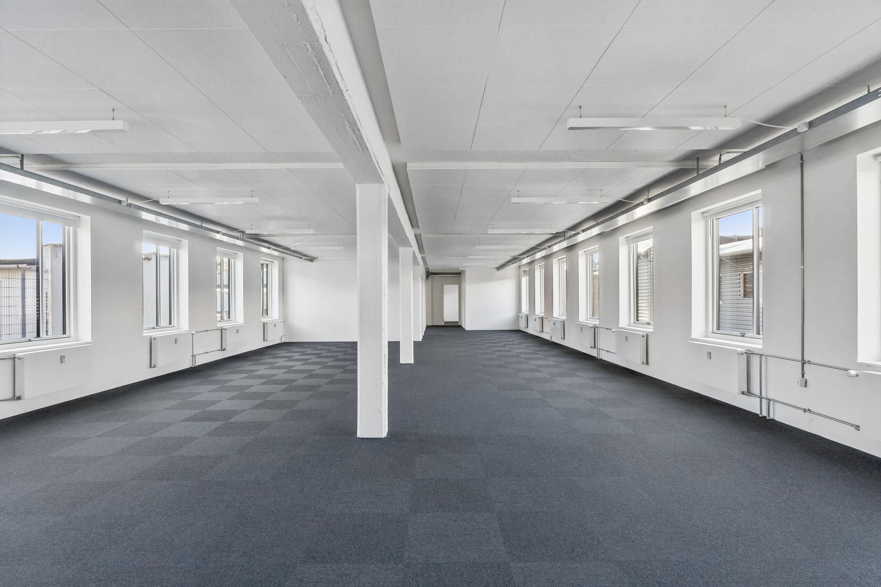 Lækre kontorlokaler på 2. sal med store vinduer og tæt på Føtex. Ingen møbler og lyse lofter. En hvid søjle står fremtrædende på gulvet.