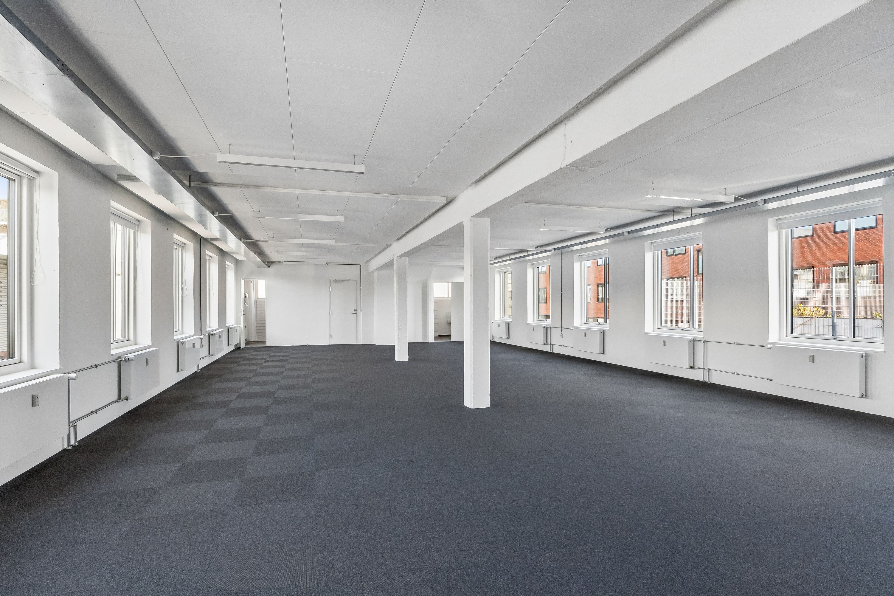 Rummelig kontorlokaler med hvide vægge og krydsvise gulvbelægning i et fredeligt miljø. Vinduer med glas og vinduesskodder og hvide søjler.