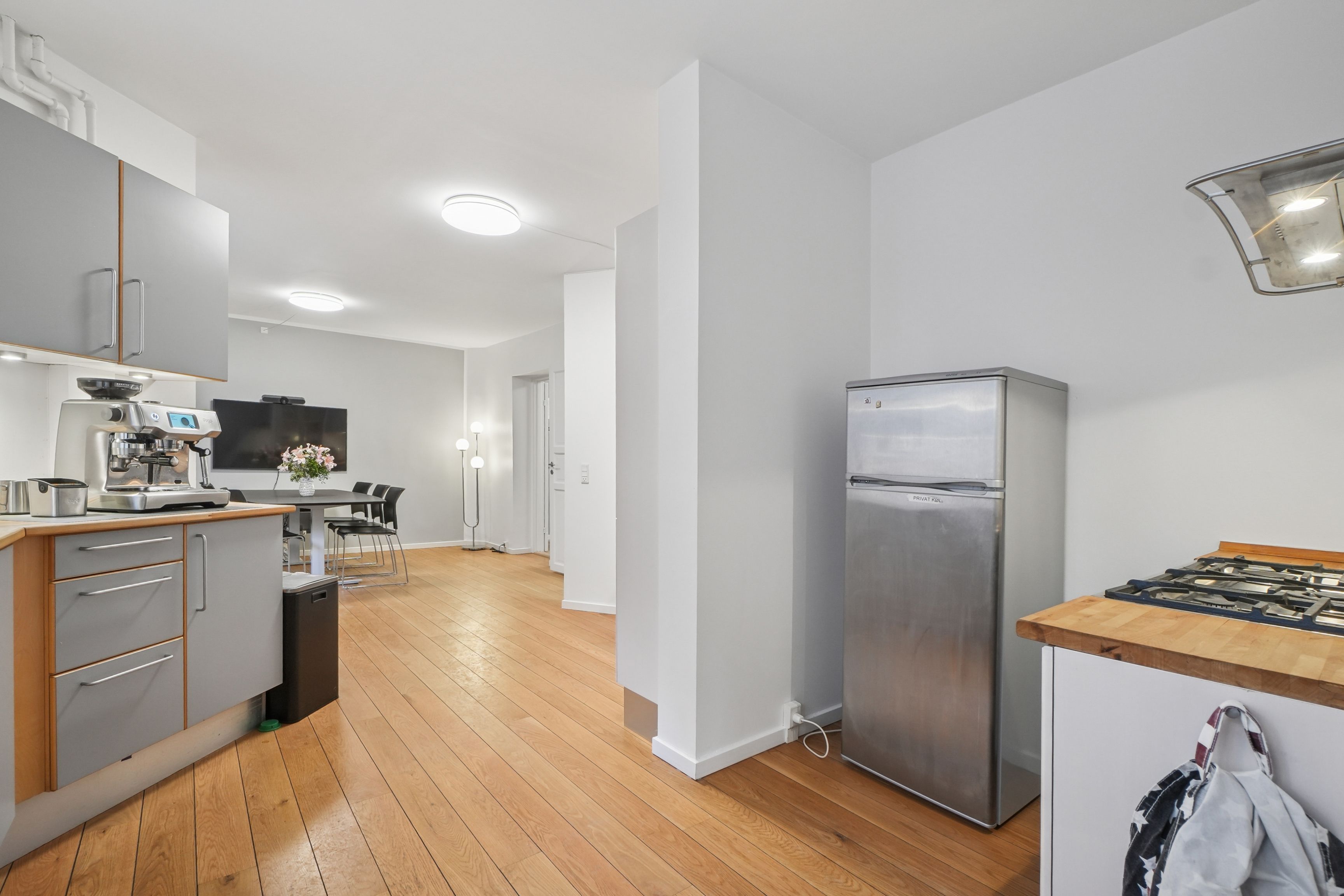 Kontor med moderne køkken, trægulv, lyse hvide vægge, indbygget køleskab, køkkenmaskiner og lysekroner