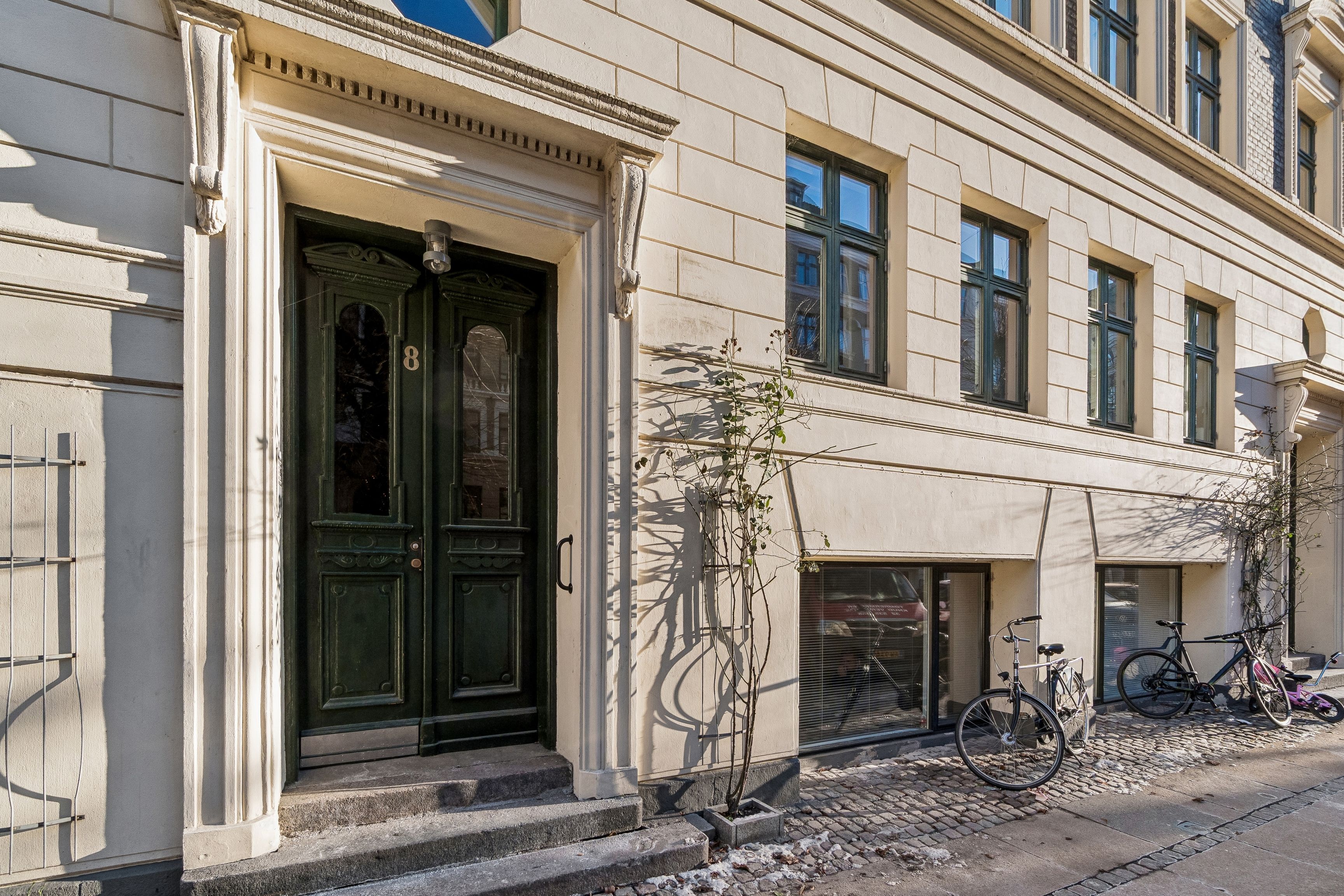 Kontor på Schleppegrellsgade 8 med lyse vinduer og trætrapper. Cykler parkeret foran og grønne døre. Lejlighed i København N med moderne og stilfuld design