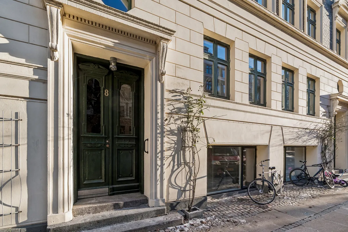 Kontor på Schleppegrellsgade 8 med lyse vinduer og trætrapper. Cykler parkeret foran og grønne døre. Lejlighed i København N med moderne og stilfuld design