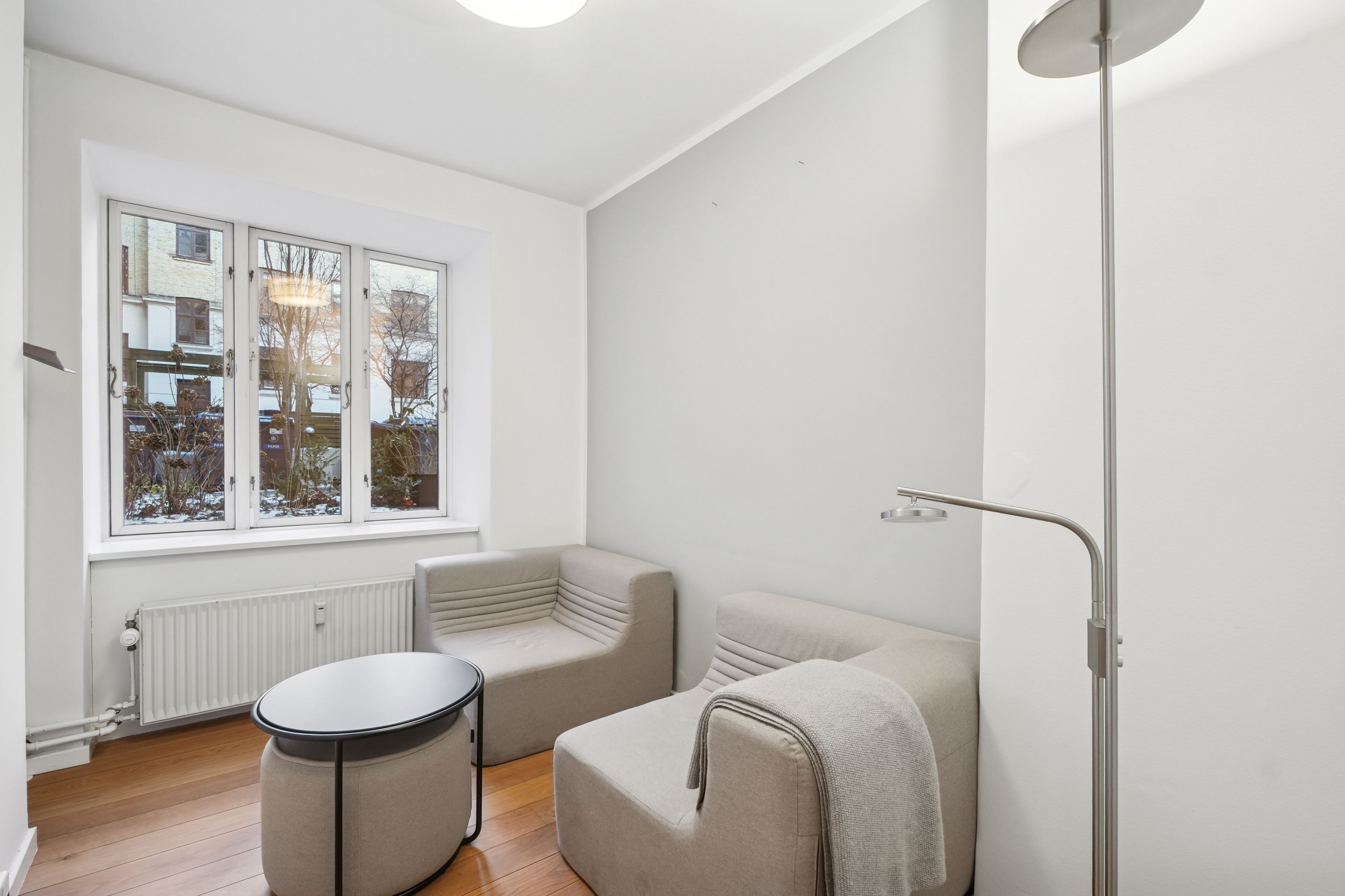 En luksuriøs og minimalistisk stue med højloft og møbler og en gulvlampe med to armer, en simpel rund sofa og en stol med en hvid tæppe