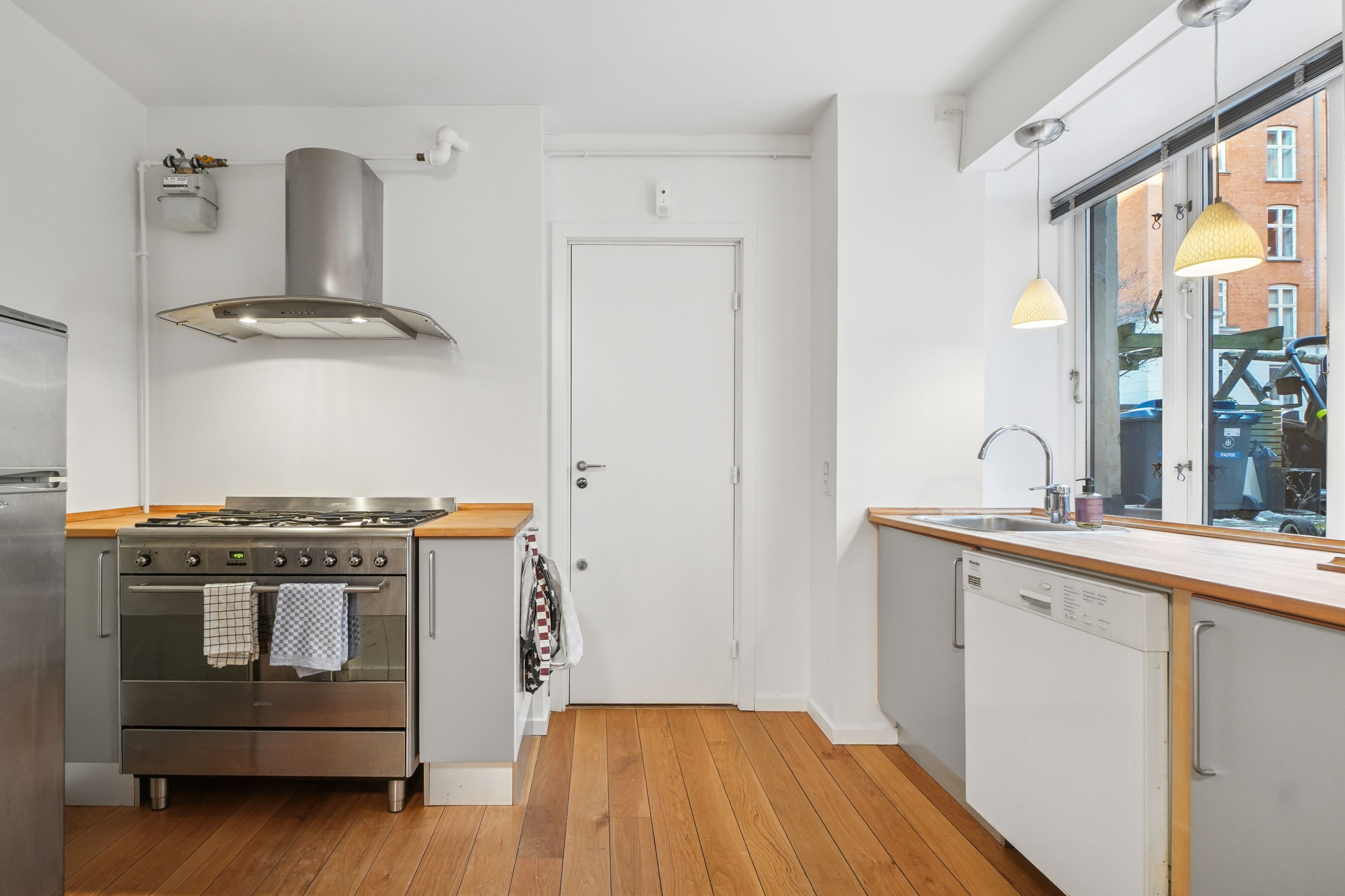 Rummelige kontorlokaler med moderne køkkenudstyret og gaskomfur, hvide vægge og trægulve samt lyse lysekroner og vinduer med udsigt til gaden