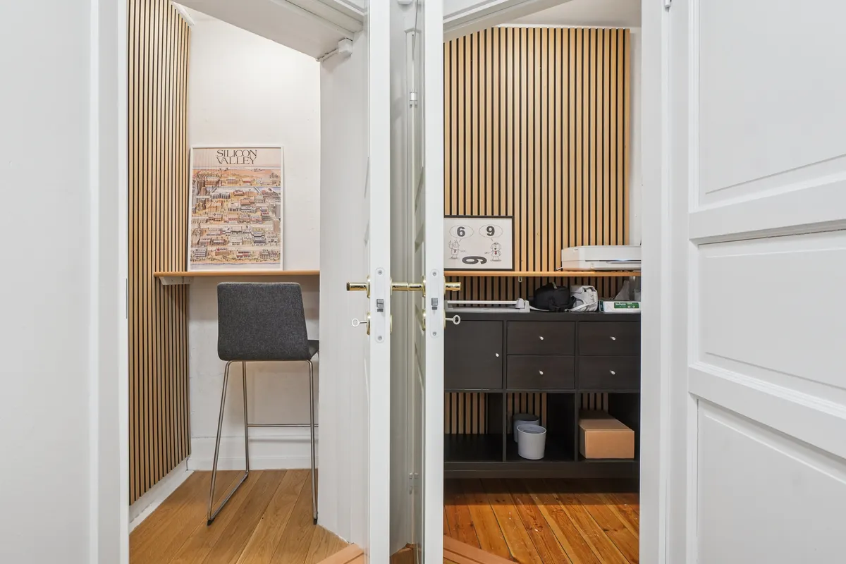 Åbne døre med indgang til et lille kontor med skrivebord, stol, hylde og et kalenderskildt med tallet 9