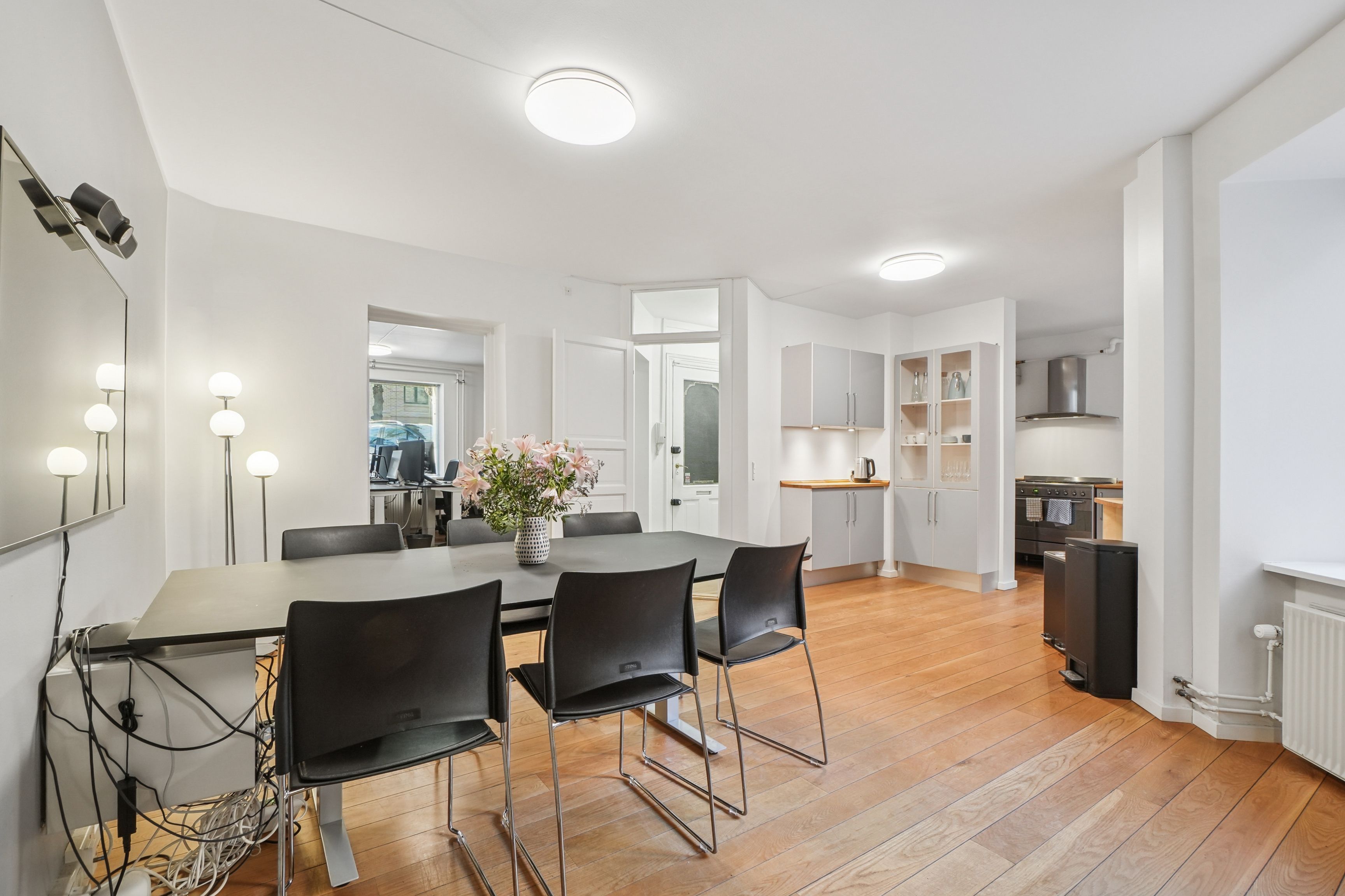 Modernt kontor med lyse gulve, hvide vægge og møbler, lysekroner og blomster i en vase på spisebordet