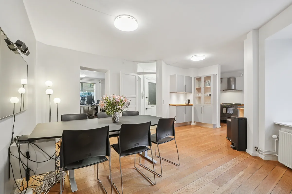 Modernt kontor med lyse gulve, hvide vægge og møbler, lysekroner og blomster i en vase på spisebordet