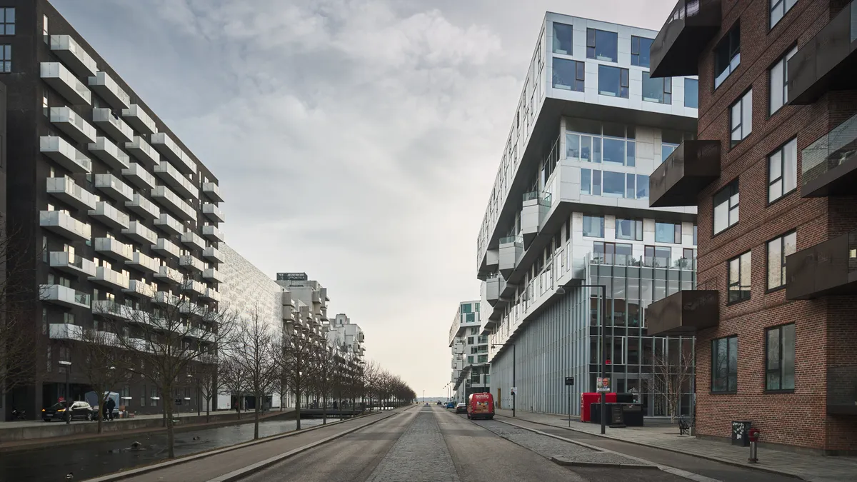Lang vej med huse, hvoraf det højeste er lavet i glas og beton, og det lavere er lavet af mursten og har mange balkoner og terrasser