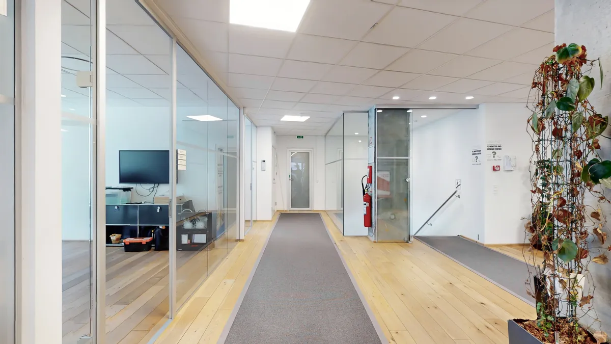 En moderne og veludstyret kontorhal med trægulv og glasvægge med et rødt ildslukker i hjørnet og en stor plante i øverste højre hjørne