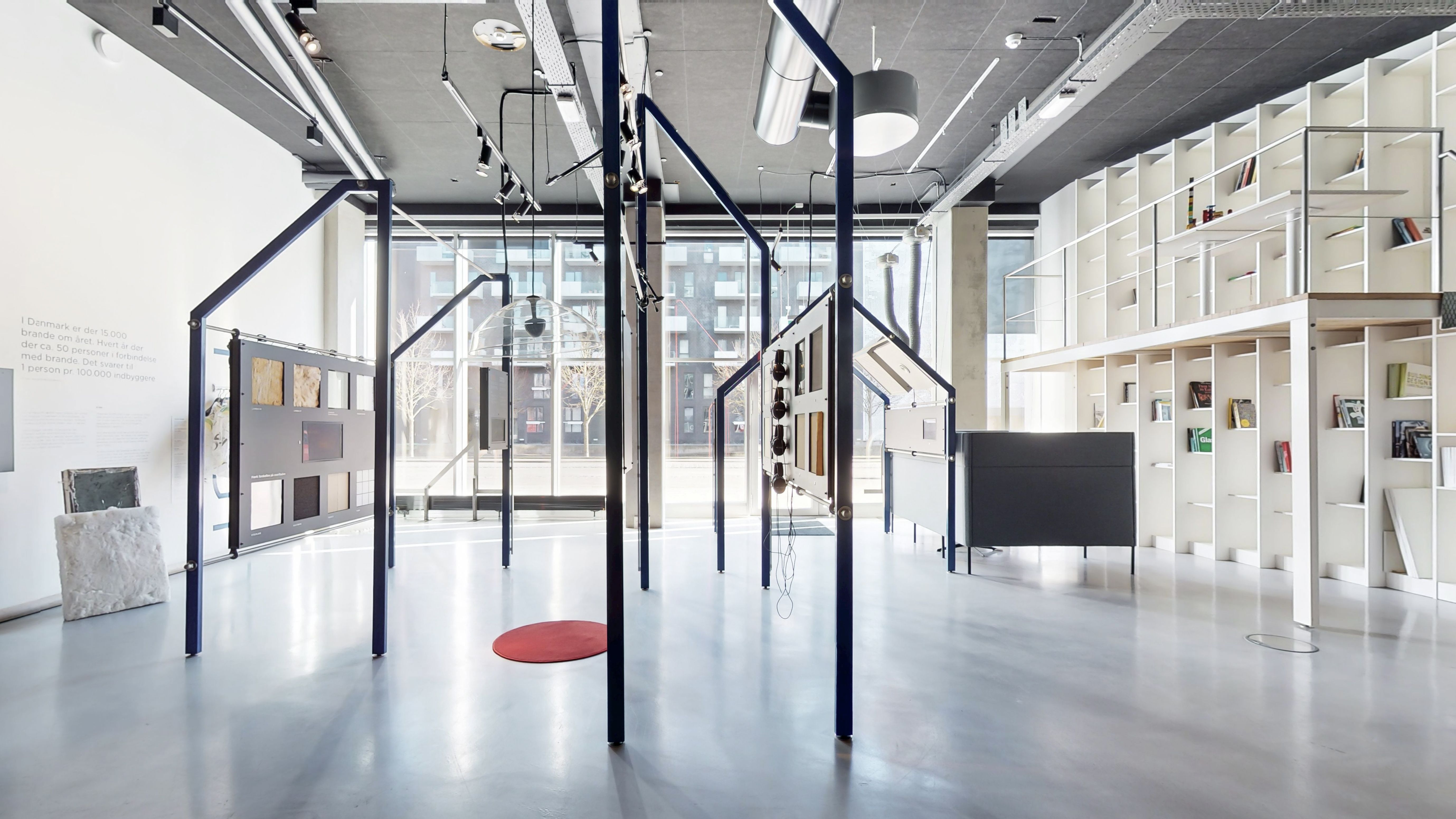 Markant og rummeligt erhvervslejemål i 8-tallet med lyse loftskroner, minimalistisk hvid indretning, glasvægge, højre hjørne med læsestue og højre side med høje hylder med bøger