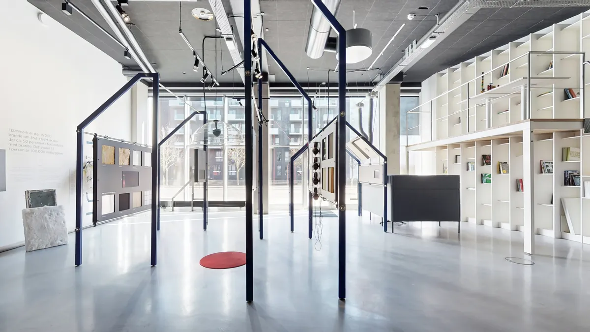 Markant og rummeligt erhvervslejemål i 8-tallet med lyse loftskroner, minimalistisk hvid indretning, glasvægge, højre hjørne med læsestue og højre side med høje hylder med bøger