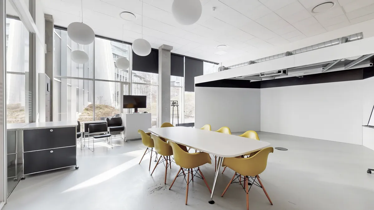 Markant og rummeligt erhvervslejemål med hvide vægge, lyse lamper og moderne møbler. Køkken med høj kvalitet og udsigt til byen. I baggrunden ses et glasvindu