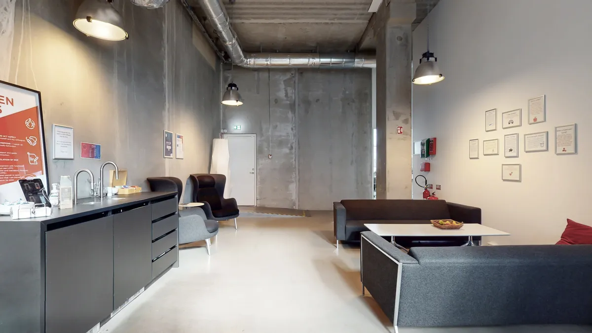 Markant og rummeligt erhvervslejemål med moderne indretning, hvidgulv, fire sovesofaer og lyse gulvvægge. En stor mængde plakater og fire hængelampe.