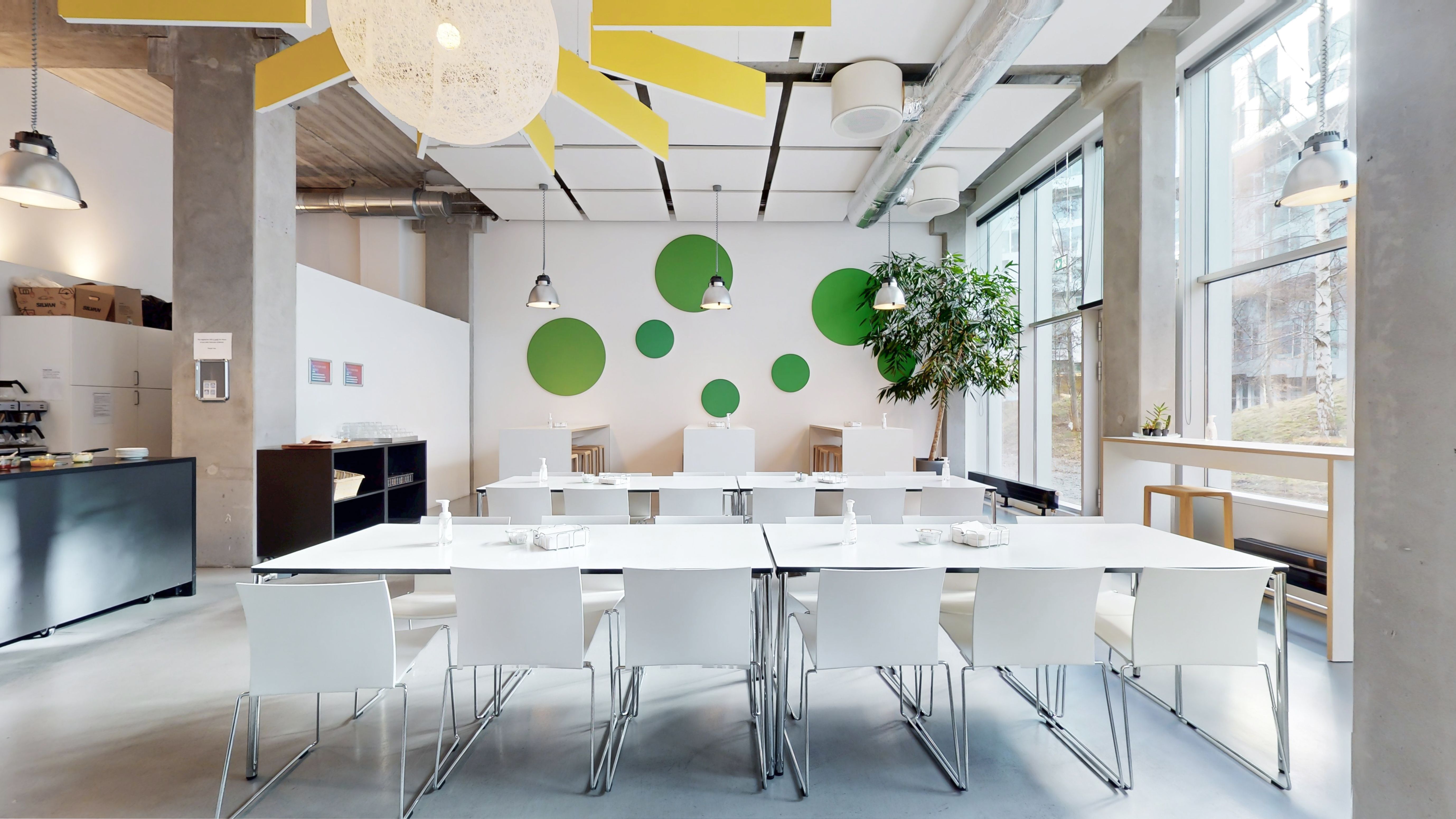 Hvidt møbelarrangement med lyse stole og lange hvide borde samt grønne cirkler i loftet og lysekroner med lyse glaskugler