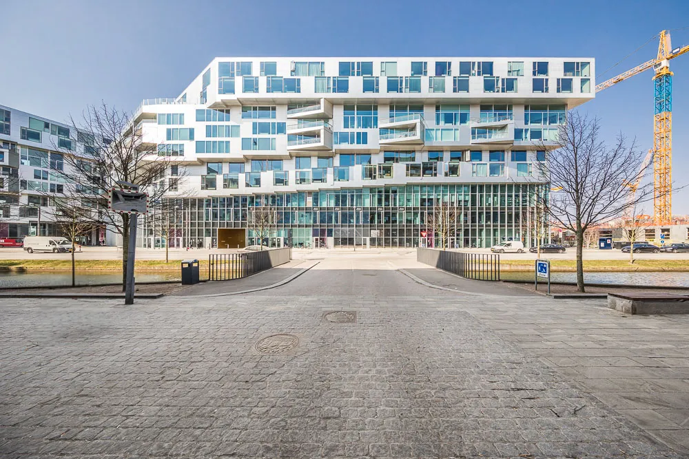 Moderne erhvervsbygning med glas og beton facader placeret i et kvarter med flotte træer og en stor byggekran