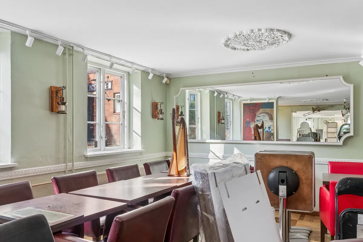 Lyst caférum med elegant indretning, store vinduer og lyse loftskroner. Faciliteter inkluderer moderne møbler, kunstværker og musikinstrumenter. Lokaler med potentiale til mange erhverv.