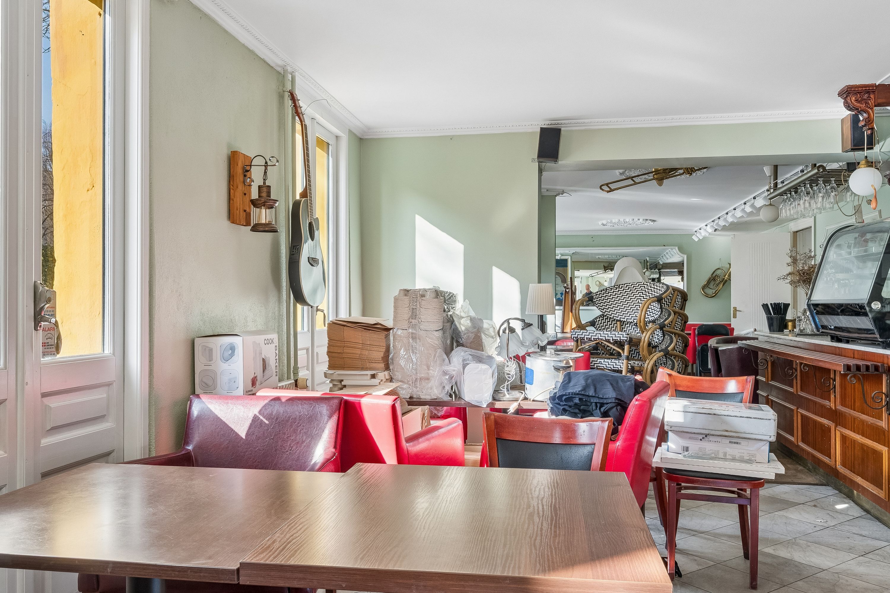 Inde i en kafe er der røde stole og borde, en bar med en kaffemaskine og stolpe, og et musikinstrument hænger på væggen