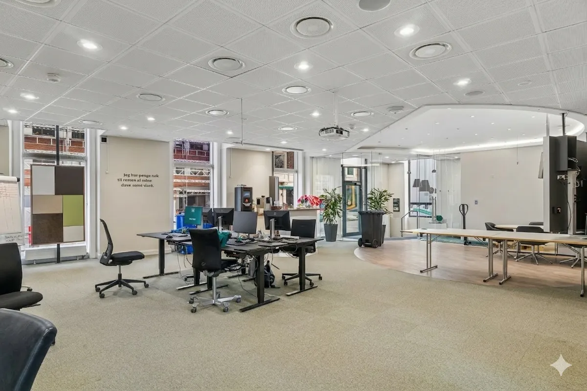 Kontor med moderne møbler og skriveborde, computere og plantepotter samt skriveborde og stolpe.