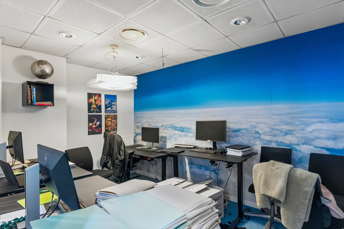 Kontor med flere skriveborde, hver med computer, stol, smykkeskabs og et jordglob samt malerier på væggen med himmel og skyer