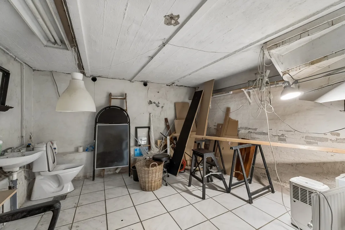 Værelse med toilet, vandhane og lysekroner, samt diverse redskaber, værktøj og materialer.