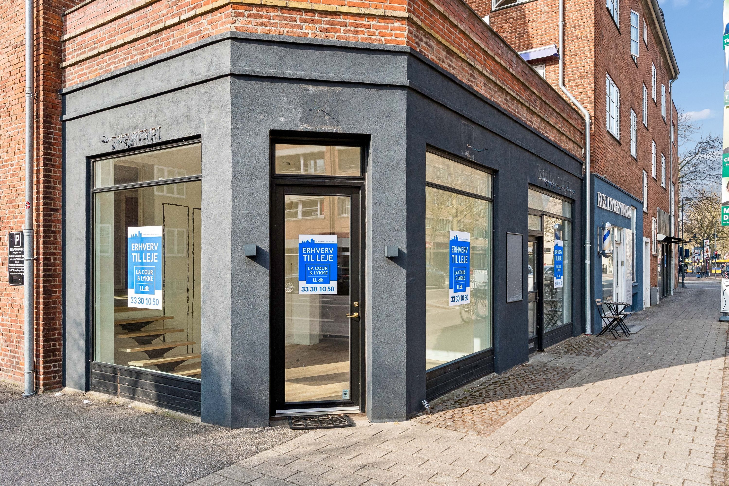 Synlig udsigt til en butik med vinduer, der viser stige og reklamepapirer med teksten Erhverv til Leje og åbningstider