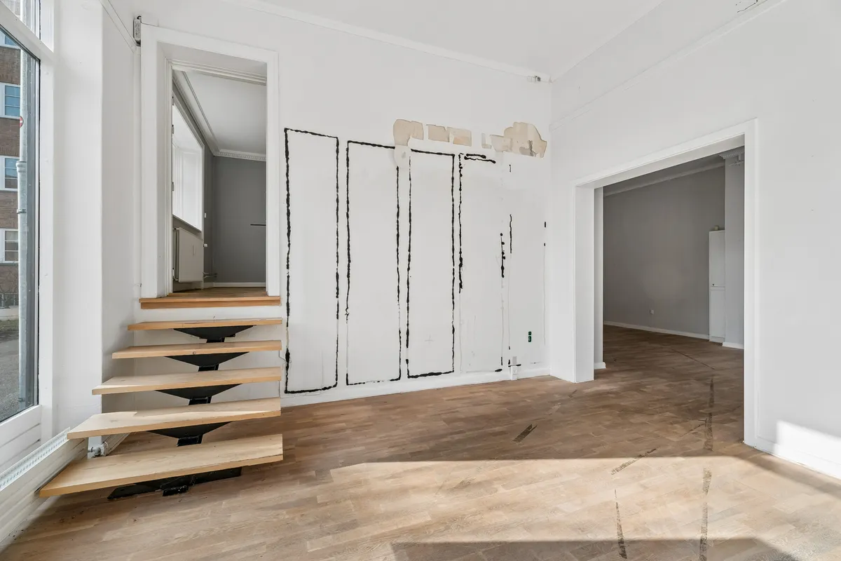 Foto af tomt lokale med hvidt panel og trægulv samt trappe i lysebrunt træ