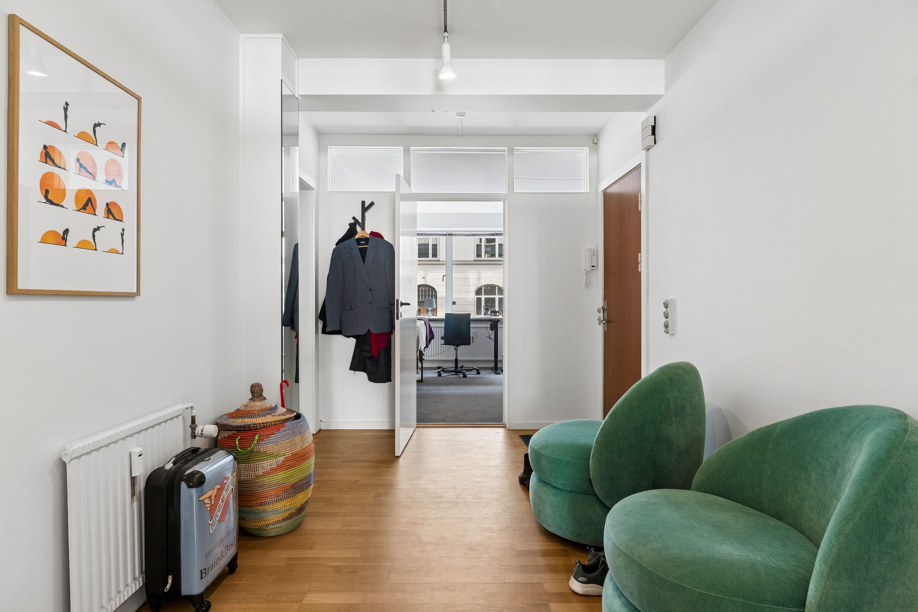 Kontor med åben dør og møbler, trægulv og hvide vægge samt møbler og kunstværk.