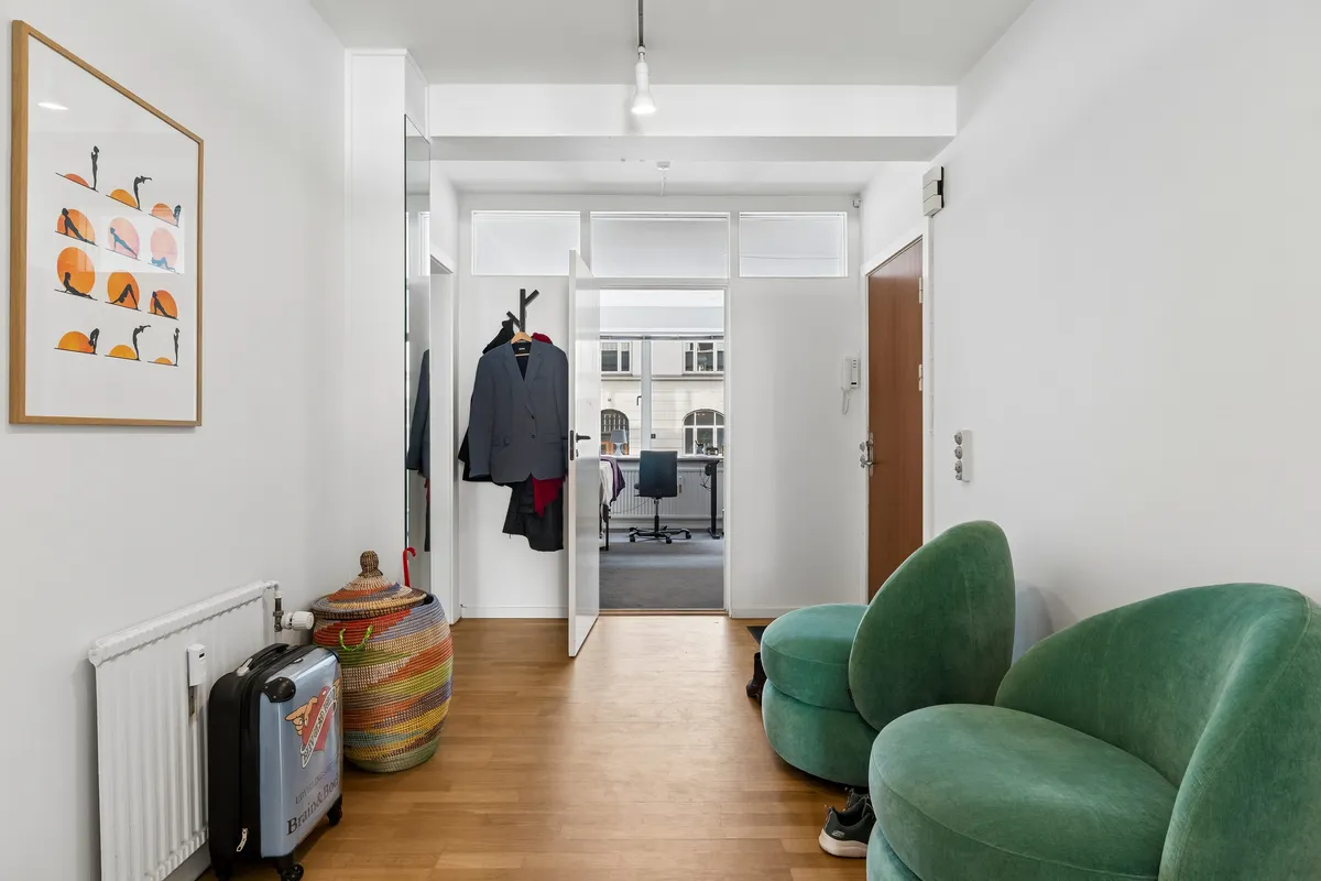 Kontor med åben dør og møbler, trægulv og hvide vægge samt møbler og kunstværk.